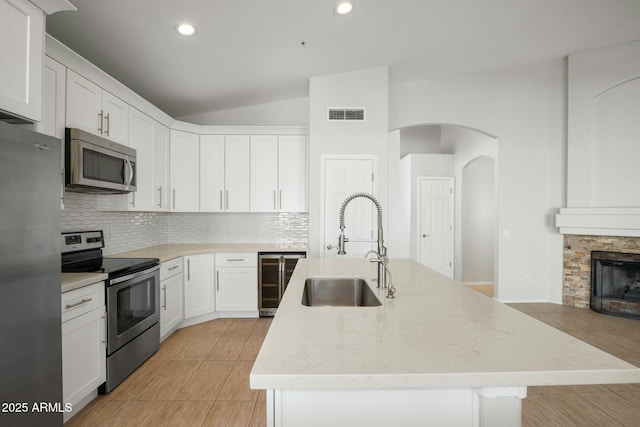 kitchen with visible vents, a sink, stainless steel appliances, wine cooler, and vaulted ceiling