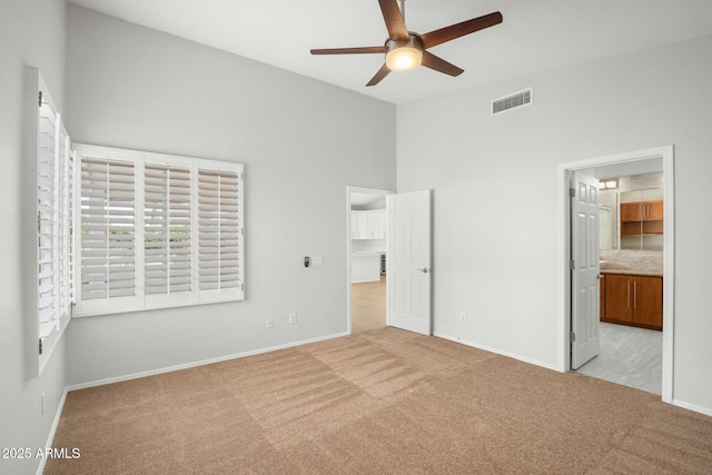 unfurnished bedroom featuring carpet, visible vents, baseboards, ensuite bath, and a high ceiling