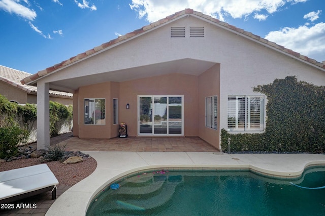 back of house featuring an outdoor pool, stucco siding, a patio, and a tiled roof