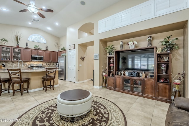 tiled living room with ceiling fan, sink, and high vaulted ceiling