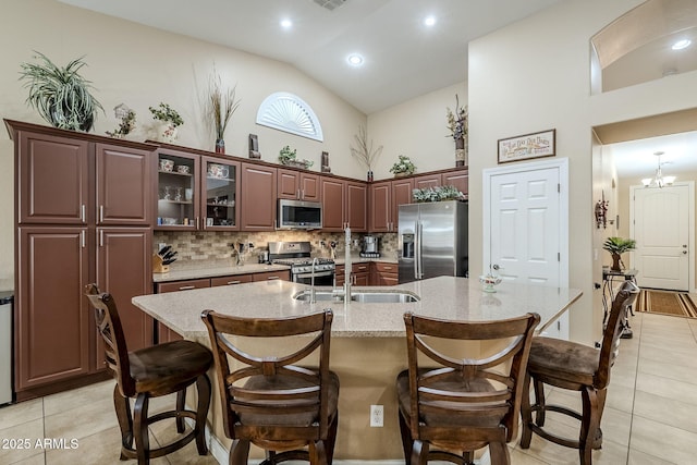 kitchen with appliances with stainless steel finishes, tasteful backsplash, sink, a kitchen island with sink, and light tile patterned floors