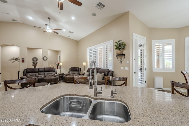 kitchen featuring ceiling fan, lofted ceiling, light stone countertops, and sink