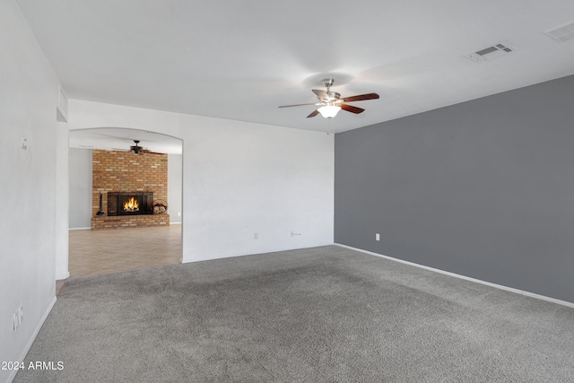 unfurnished room with light carpet, a brick fireplace, and ceiling fan