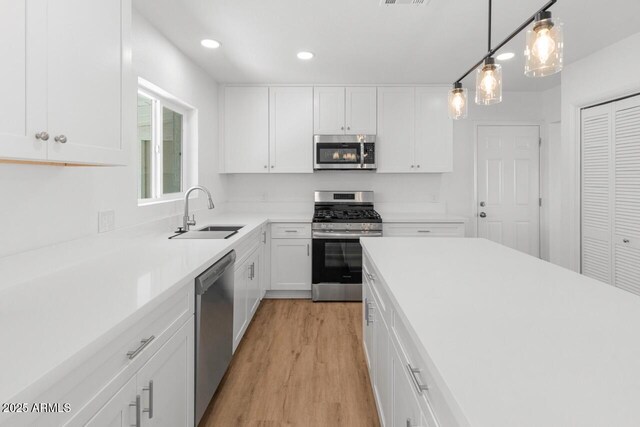 6610 N 15th Ave, Phoenix, AZ 85015 - kitchen featuring white cabinets, light wood-type flooring, stainless steel appliances, and a sink