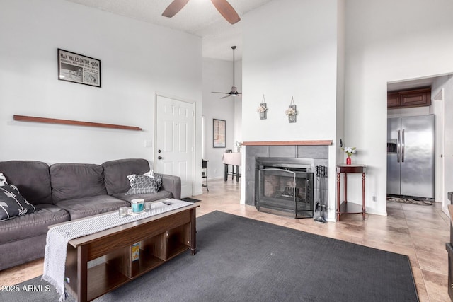 living room with ceiling fan, a towering ceiling, and a fireplace