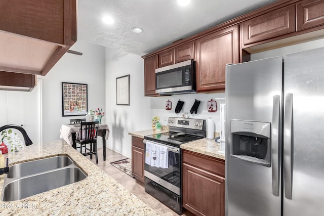 kitchen with light stone countertops, a textured ceiling, stainless steel appliances, light tile patterned floors, and sink