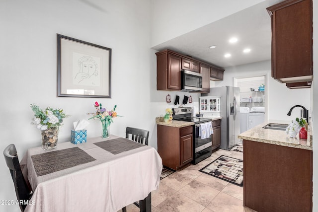 kitchen with light stone countertops, stainless steel appliances, light tile patterned floors, washer and dryer, and sink