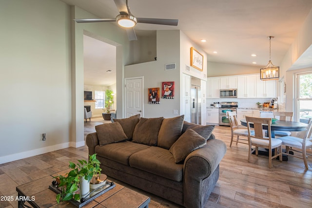 living room featuring high vaulted ceiling, ceiling fan with notable chandelier, visible vents, and light wood-type flooring