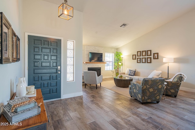 foyer entrance with high vaulted ceiling, a stone fireplace, wood finished floors, baseboards, and visible vents