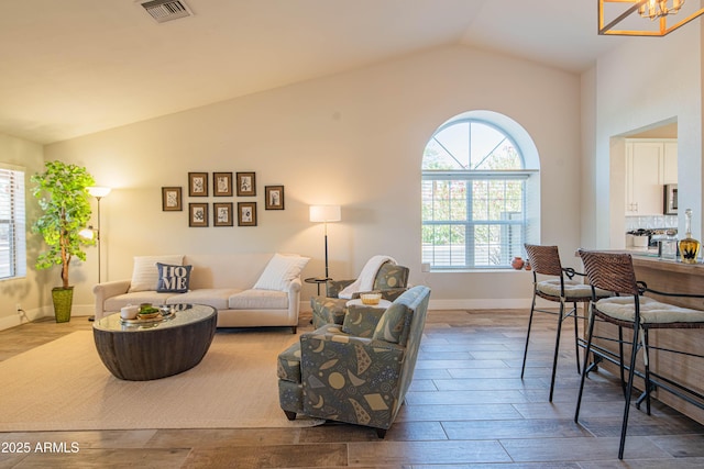 living room with baseboards, visible vents, an inviting chandelier, lofted ceiling, and wood finished floors