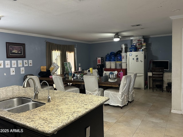 kitchen featuring sink, a center island with sink, ornamental molding, white fridge, and light stone countertops