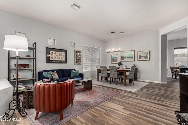 living room with an inviting chandelier, baseboards, visible vents, and wood finished floors