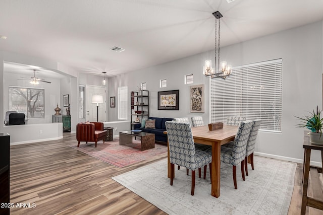 dining area featuring ceiling fan with notable chandelier, wood finished floors, visible vents, and baseboards