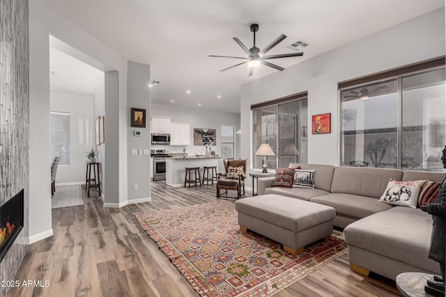 living area with a warm lit fireplace, visible vents, baseboards, a ceiling fan, and light wood-style flooring