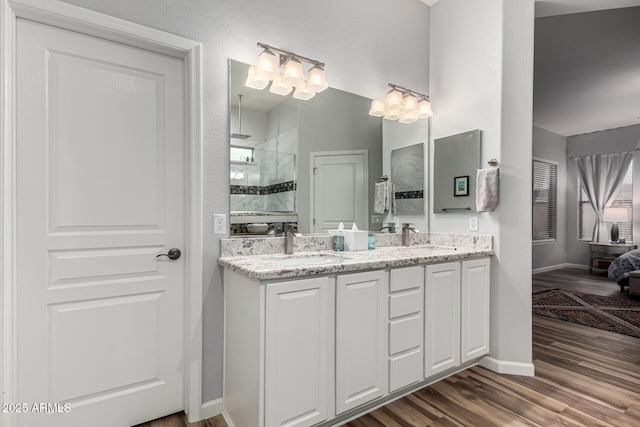 bathroom featuring double vanity, wood finished floors, a sink, a walk in shower, and baseboards