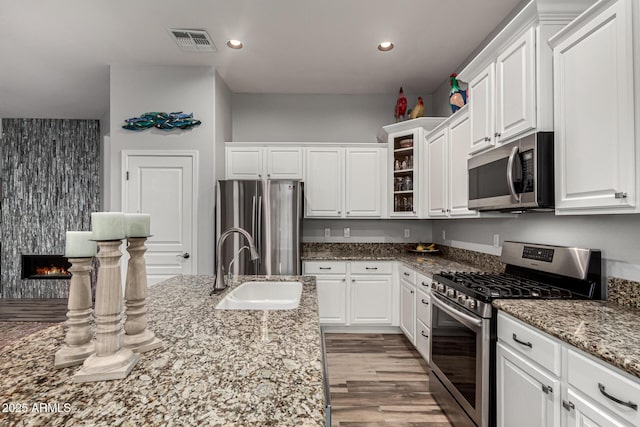 kitchen featuring a large fireplace, a sink, visible vents, white cabinetry, and appliances with stainless steel finishes