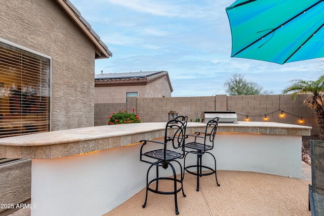 view of patio featuring exterior kitchen, a grill, fence, and outdoor dry bar