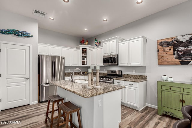 kitchen with stone countertops, white cabinetry, stainless steel appliances, and a sink