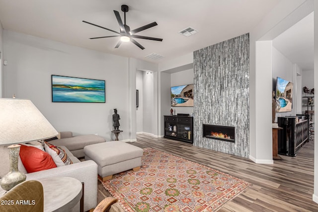 living room with a fireplace, visible vents, a ceiling fan, wood finished floors, and baseboards