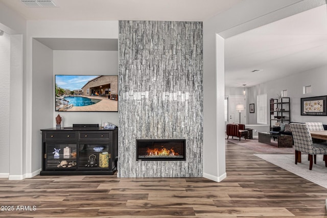 living area with a large fireplace, wood finished floors, visible vents, and baseboards