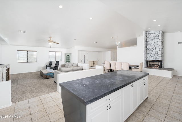 kitchen with a stone fireplace, white cabinets, ceiling fan, a center island, and light tile patterned floors