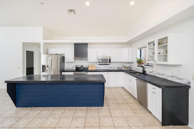 kitchen featuring stainless steel appliances, white cabinets, wall chimney range hood, a center island, and sink