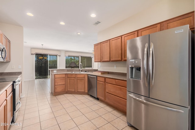 kitchen featuring kitchen peninsula, hanging light fixtures, sink, light tile patterned floors, and appliances with stainless steel finishes