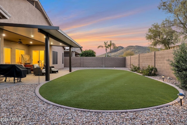 yard at dusk with a patio area, ceiling fan, a mountain view, and an outdoor hangout area