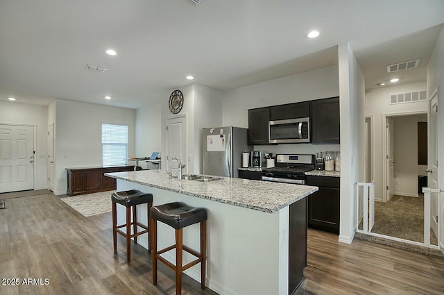 kitchen with appliances with stainless steel finishes, a breakfast bar, sink, light hardwood / wood-style flooring, and an island with sink