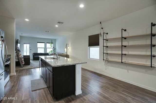 kitchen featuring light stone countertops, dark hardwood / wood-style flooring, a kitchen island with sink, and sink