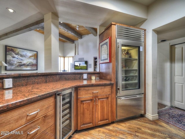 kitchen featuring high quality fridge, vaulted ceiling with beams, beverage cooler, dark stone counters, and light hardwood / wood-style floors