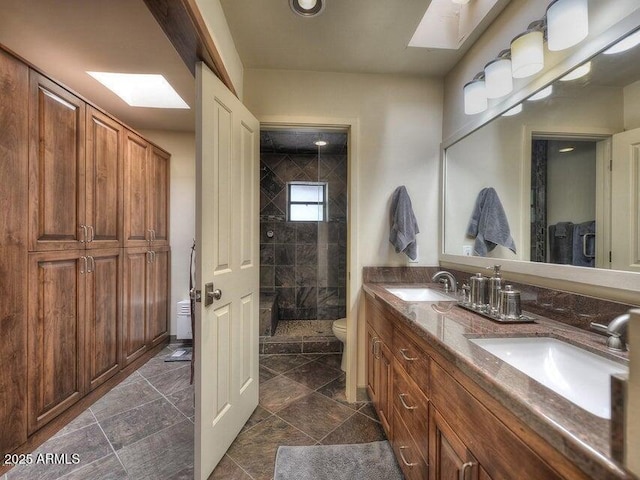 bathroom featuring vanity, toilet, a skylight, and a tile shower