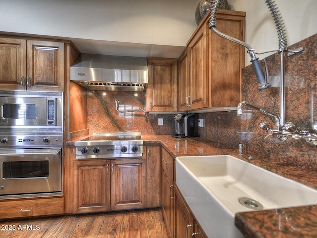 kitchen with sink, tasteful backsplash, appliances with stainless steel finishes, hardwood / wood-style floors, and wall chimney range hood