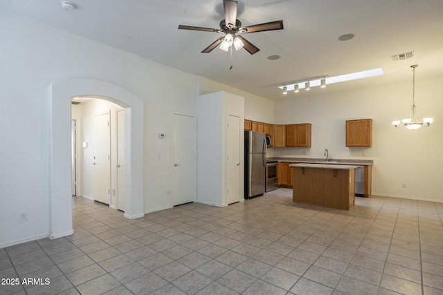 kitchen featuring light tile patterned flooring, decorative light fixtures, a center island, stainless steel appliances, and ceiling fan with notable chandelier