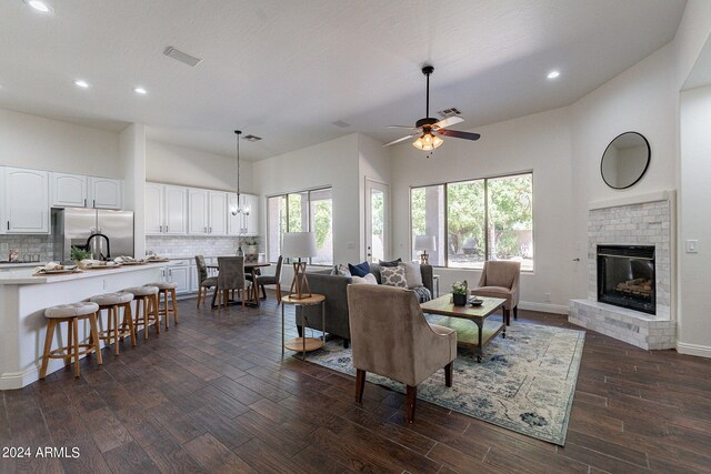 living room featuring a brick fireplace, ceiling fan, a high ceiling, and dark wood-type flooring