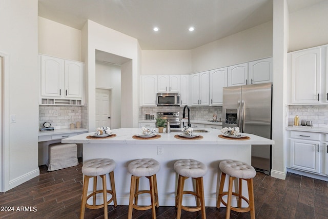 kitchen featuring white cabinetry, decorative backsplash, a center island with sink, appliances with stainless steel finishes, and dark hardwood / wood-style flooring