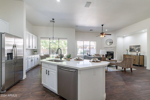 kitchen featuring an island with sink, sink, a stone fireplace, white cabinetry, and appliances with stainless steel finishes