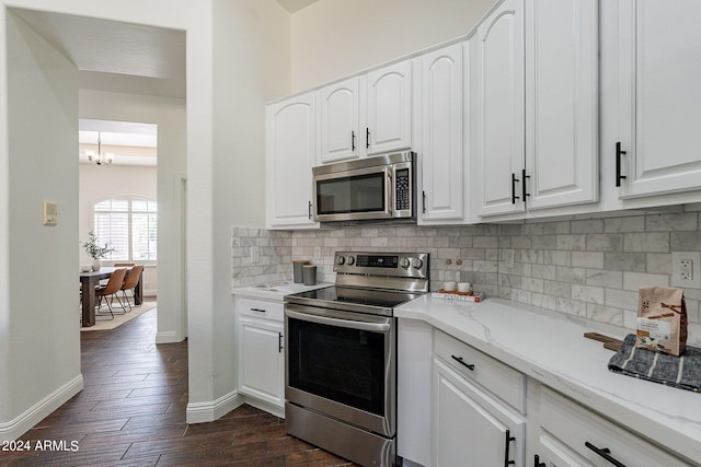 kitchen with light stone counters, white cabinets, a chandelier, appliances with stainless steel finishes, and dark hardwood / wood-style flooring