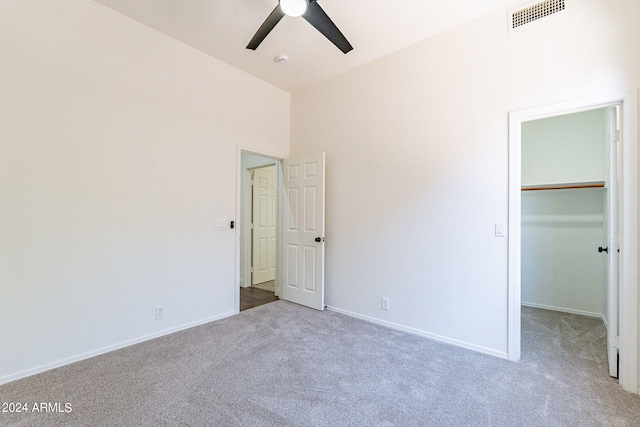 unfurnished bedroom with light colored carpet, ceiling fan, a walk in closet, and a closet