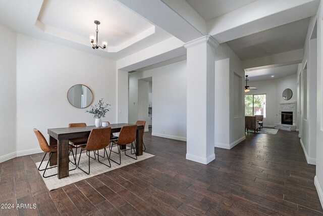 dining area with ceiling fan with notable chandelier, a tray ceiling, decorative columns, and dark hardwood / wood-style flooring