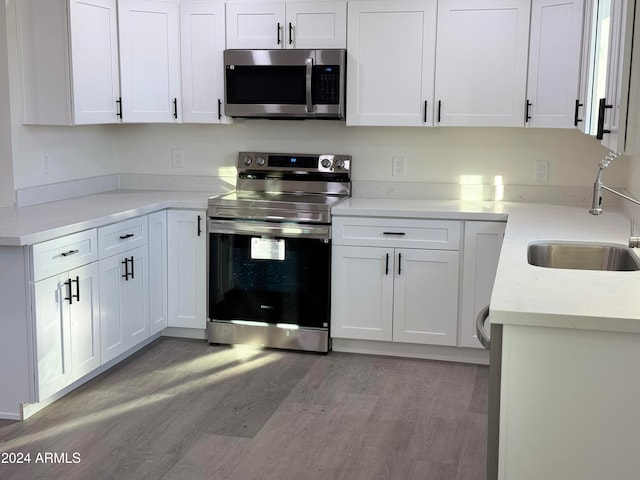 kitchen with appliances with stainless steel finishes, light stone countertops, sink, white cabinets, and light hardwood / wood-style flooring