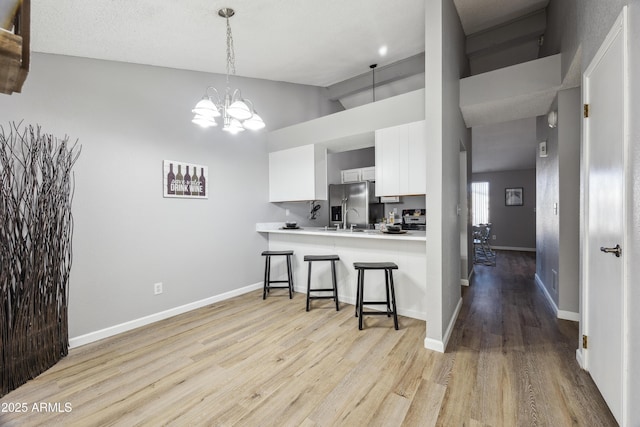 kitchen with a breakfast bar, stainless steel fridge, kitchen peninsula, white cabinets, and a high ceiling