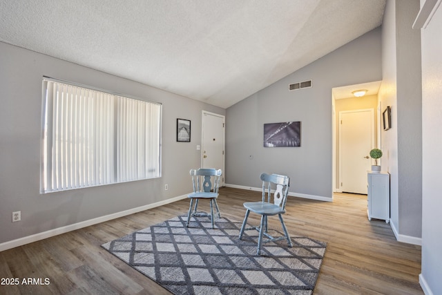 sitting room with vaulted ceiling, hardwood / wood-style floors, and a textured ceiling