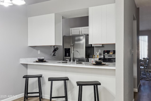 kitchen featuring sink, a breakfast bar area, white cabinets, and stainless steel refrigerator with ice dispenser