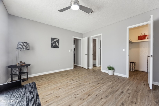 bedroom featuring a spacious closet, a textured ceiling, light wood-type flooring, a closet, and ceiling fan