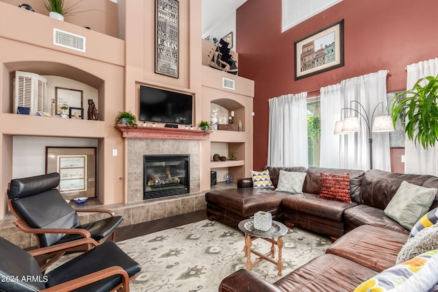 living room featuring built in shelves, a tile fireplace, hardwood / wood-style flooring, and a towering ceiling