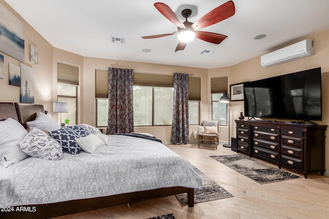 bedroom with light hardwood / wood-style floors, ceiling fan, multiple windows, and a wall mounted air conditioner