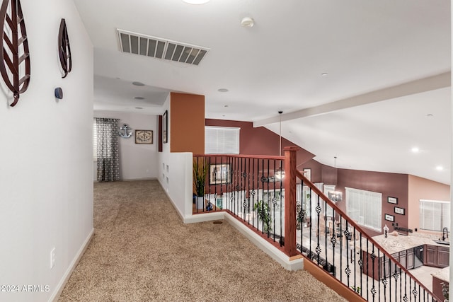 hallway with light colored carpet, plenty of natural light, and lofted ceiling with beams