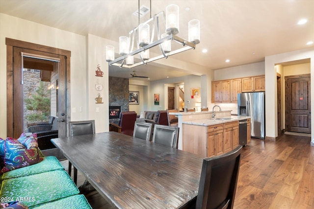 dining space with a large fireplace, sink, wood-type flooring, and an inviting chandelier