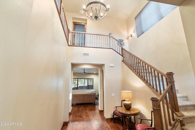 staircase with wood-type flooring, ceiling fan with notable chandelier, and a high ceiling